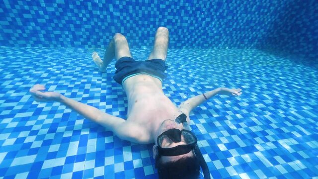 Underwater scene of a man lying at the bottom of the pool making bubble rings.