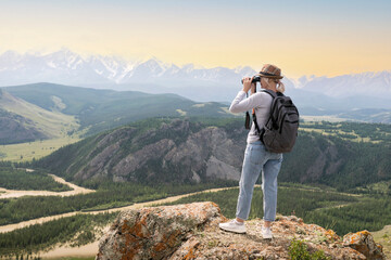 Hiker with backpack looking in binoculars on top of mountains at sunset.