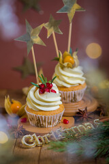 Christmas cupcakes with vanilla frosting, cranberries and rosemary on wooden background. Selective focus