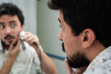 young man with beard trimming his beard with a beard trimmer