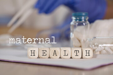 Word MATERNAL HEALTH composed of wooden dices. Pills, documents and a pen in the background.