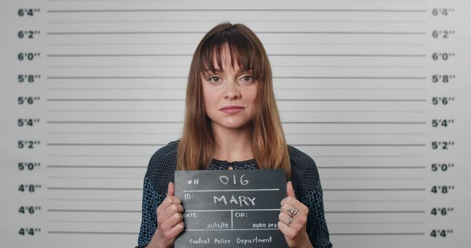 Portrait of adult woman with forelock holding sign for photo in police department. Crop view of pretty female criminal posing, raising head and looking to camera.Concept of mugshot.