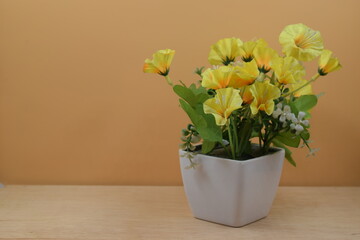 flor amarilla en florero blanco, sobre superficie de madera y fondo naranja. en posición horizontal y alineada a la izquierda