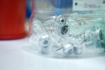 Empty hazard materials container for used vaccine bottles after vaccinate to person for corona virus (COVID-19) prevention. Piles of glass bottles for recycling.