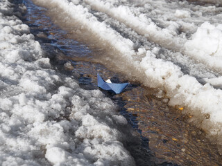 Paper boat sails through meltwater on spring day