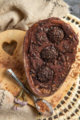 Chocolate Easter egg stuffed with brigadeiro and accompanied by decorative elements and on a wooden support in the shape of a heart and gray background