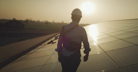 Maintenance assistance technical worker in uniform smiling satisfied of his work after checking operation and efficiency photovoltaic solar panels on roof at sunset.Concept of renewable green energy.