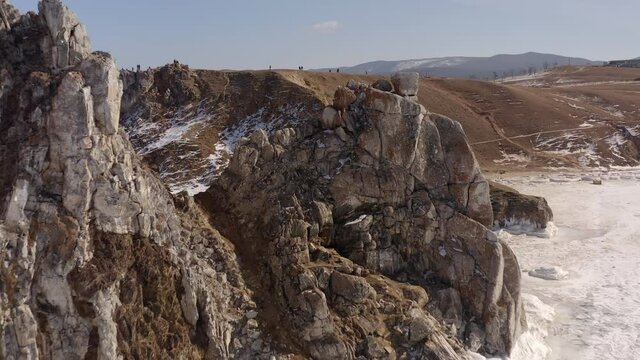 Aerial view Drone departs chamanka rocks on Olkhon Island. Frozen Lake Baikal in the daylight. Drone flies from Rock Burkhan. Winter landscape.