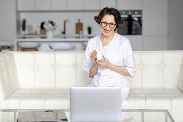 Elderly woman doctor wearing white uniform talking online with patient, making video call