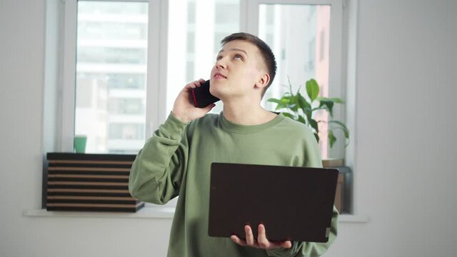 Young student uses laptop and smartphone while standing in the room