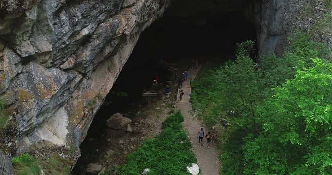 Kapova cave in Nature Reserve Shulgan-Tash. The entrance is huge arch with river flows out of ground. Limestone karst cave in the Burzyansky District of Bashkortostan. Aerial drone view at summer day