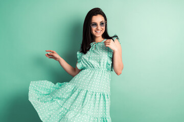 Smiling girl in a light spring dress on a mint background. The girl's dress flies to the sides, the...