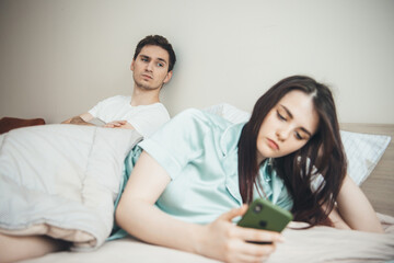 Jealous caucasian man is looking at his wife while she is chatting with somebody on mobile