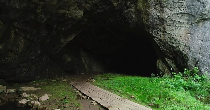 Kapova cave in Nature Reserve Shulgan-Tash. The entrance is huge arch with river flows out of ground. Limestone karst cave in the Burzyansky District of Bashkortostan. Aerial drone view at summer day