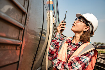 Portrait of beautiful woman engineering using walkie talkie and with wear hardhat in front of train station. Preparation for train mechanical operation.