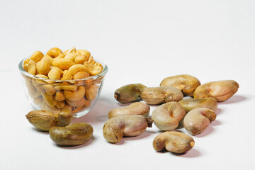 Cashew nuts in clear glass cup and unpeeled cashews on white background