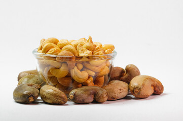 Cashew nuts in clear glass cup and unpeeled cashews on white background
