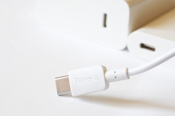 Fototapeta premium A white usb type-c connector with a wire lies against a light background next to two matching white connectors - a power supply and a dongle. The concept of data transmission. Macro
