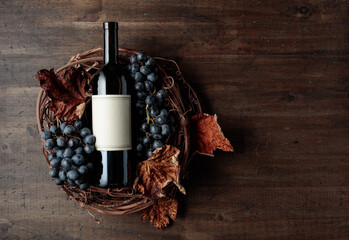 Bottle of red wine with grapes and dried vine leaves on an old wooden background.