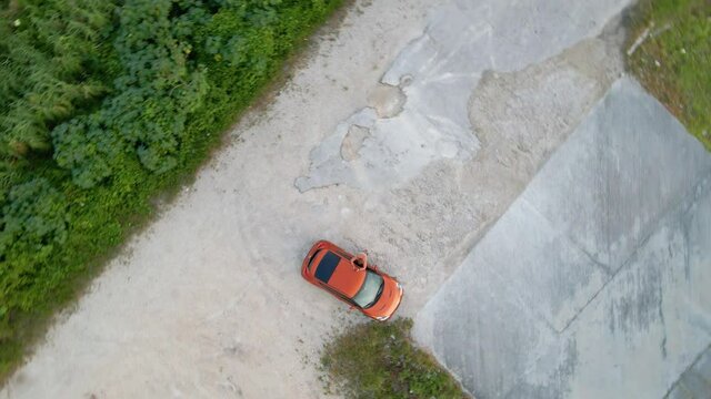 RELEASE!! Aerial view above a man and his orange car parked at a parking lot near a river, sunny evening - screwdriver, drone shot