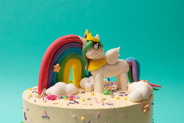 Pastel de cumpleaños de Unicornio rosa y arcoiris sobre fondo azul aqua cerca