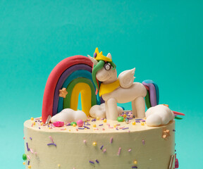 Pastel de cumpleaños de Unicornio rosa y arcoiris sobre fondo azul aqua cerca 2
