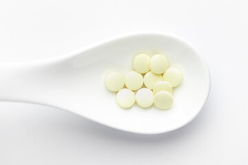Macro Close up of medicinal or herbal pale yellow pill on a white ceramic spoon. Top view, white background.