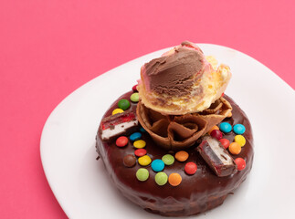 Dona con barquillo y bola de helado, cubierta de dulces sobre fondo rosa