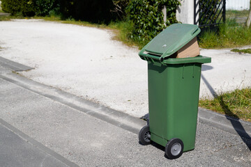 Rolling green trash can overflowing bag wheelie in street road city