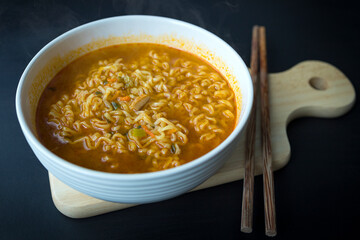 Korean ramen (ramyun) spicy instant noodle with wooden chopsticks on wooden cutting board on black wooden table.