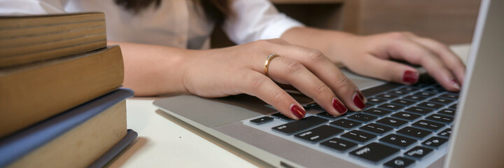 Working by using a laptop computer on wooden table. Hands typing on a keyboard.