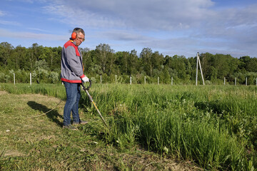 Man mows the grass with a trimmer, tall grass in a meadow, handmade in the garden.