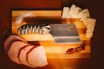 Top down photo of knife, cleaver, with food and spices, ham, cheese, salt, peper.