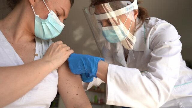 Close-up on a doctor in sterile and protective clothing injecting a covid-19 vaccine into the shoulder of a young woman with a worried expression. Vaccination time. Global pandemic