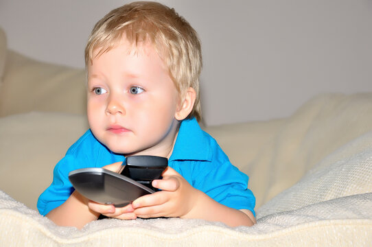 Cute kid watching tv, sitting in a very comfortable and soft chair, with a remote control