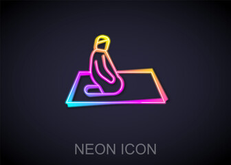 Glowing neon line Muslim man prays on the carpet icon isolated on black background. Vector