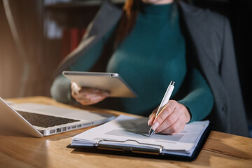 Women working on tablet and laptop on the table at the office with information documents.