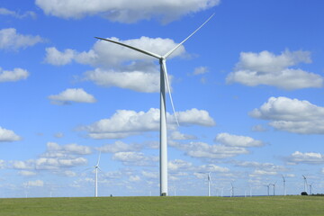 Electric windmill in a pasture with blue sky, white clouds, and green grass in the summer east of Wilson Kansas USA out in the country.