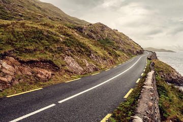 Small narrow asphalt road in a mountains by a lake, low clouds cover mountains peaks, fog descending. Scene in Connemara, Ireland Travel concept. Irish landscape.