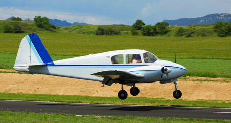 View of sports airplane in motion over runway on background with picturesque landscape.