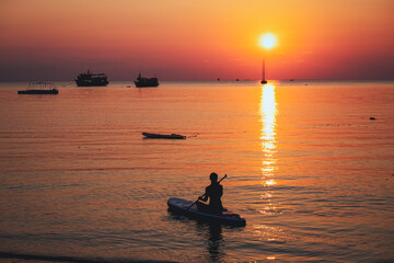 Silhouette image of a young woman sitting on stand up paddle board in the sea before sunset
