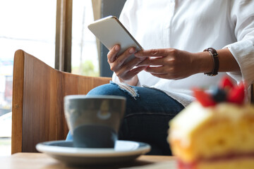 Closeup image of a  woman holding and using mobile phone while sitting in cafe