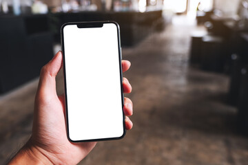 Mockup image of a man holding black mobile phone with blank white screen in cafe