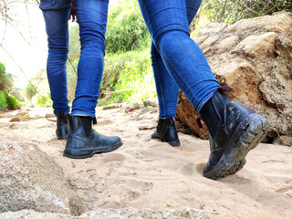 Rear view low section of couple in jeans walking on dirt trail, focus on hiking boots.