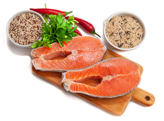 Salmon filet on a wooden board. Garnished with herbs and spices. Next to them are cups of wild rice and quinoa. White background. Isolated. Close-up. View from above.