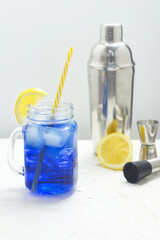Hawaiian Blue Lagoon summer alcoholic cocktail with ice in glass jar. Bartender equipment shaker, jigger and muddler