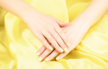 Female hands with yellow manicure on a yellow silk background.Lemon color manicure