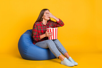 Full size photo of young scared afraid girl cover face sit armchair watch horror movie isolated on yellow color background