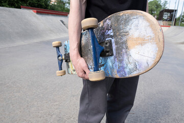 man holds a skateboard in his right hand on a background of a skatepark