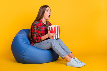 Full size profile photo of impressed brunette long hairdo lady hold pop corn wear red shirt jeans lie on bag isolated on yellow background